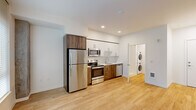 Located at 1670 SW Alder St in Portland's vibrant West End neighborhood, this efficiently designed unit offers a thoughtful, modern layout across a single floor. Light hardwood flooring runs throughout, lending warmth and visual continuity to the open-plan living space. Large windows allow natural light to fill the living area, where an exposed concrete structural column adds an industrial architectural accent alongside clean white walls.

The kitchen is a standout feature, outfitted with a full suite of stainless steel appliances — including a refrigerator, electric range, over-the-range microwave, and dishwasher — paired with two-tone cabinetry combining crisp white upper cabinets and rich wood-toned lower cabinets. White countertops and recessed lighting complete the polished, contemporary look.

Tucked conveniently off the main living area is a stacked washer and dryer unit, offering the practicality of in-unit laundry. The bathroom features a clean, all-white walk-in shower enclosure with chrome fixtures, reflecting the unit's consistent modern aesthetic. Recessed lighting throughout the space ensures a bright and welcoming atmosphere, while the efficient floor plan makes excellent use of every square foot.