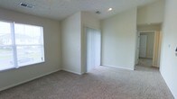 This single-story space features a clean, straightforward design with neutral beige walls and wall-to-wall carpeting that creates a warm, understated atmosphere. The room is finished with white baseboards and a textured ceiling, contributing to a simple yet practical aesthetic. A window along one wall allows natural light to filter into the space, brightening the interior. A set of vertical blinds covers what appears to be a closet or secondary access point, offering both storage and flexibility. Recessed lighting in the ceiling supplements the natural light, ensuring the space remains well-lit. The open layout provides a versatile foundation that can accommodate a variety of furniture arrangements and uses. The walls are smooth and move-in ready, with electrical outlets positioned at standard intervals. Overall, the space presents a functional, no-frills environment with neutral finishes that serve as a blank canvas for personalization.