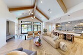 Located at 55 Ridge Ln in Waltham, MA, this community lounge is a thoughtfully designed single-floor space that blends comfort, functionality, and contemporary style. The centerpiece of the lounge is a dramatic vaulted ceiling accented by exposed natural wood beams, flooded with natural light from large black-framed windows and glass doors that offer views of the outdoor pool area. Light hardwood flooring flows throughout, unifying the open-plan layout with a warm, cohesive aesthetic.

The main lounge area features generous seating arrangements, including plush sofas, curved accent chairs, and built-in banquette nooks with textured gray upholstery, alongside a wall-mounted television and a striking multi-globe chandelier. A hallway lined with navy blue settees and a bold gold pendant light connects the lounge to a series of four glass-walled private offices with black metal framing, ideal for focused work or meetings.

The kitchenette area is a standout feature, showcasing a large marble-topped island with bar seating, warm wood cabinetry, open shelving against a textured tile backsplash, pendant lighting, and modern appliances including a coffee station and a water dispenser. Curated greenery and tasteful artwork are placed throughout, contributing to the lounge's welcoming and upscale ambiance.