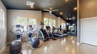 Located at 5715 Red Leaf Dr S in Salem, Oregon, this dedicated exercise room is a thoughtfully designed fitness space that combines functional layout with striking architectural details. The room's vaulted ceiling, finished in a bold dark hue, creates a dramatic contrast against the light-toned walls, while ceiling fans with pendant-style fixtures ensure comfortable airflow throughout workouts. Polished concrete floors run the length of the space, offering a durable and easy-to-maintain surface.

Natural light pours in through multiple large windows positioned along the perimeter, offering views of surrounding greenery and lending the space an open, energizing atmosphere. The cardio area is well-appointed with treadmills, an elliptical, a stair climber, and a stationary bike, all arranged to maximize usability. A dedicated strength training zone features a cable/rack system, a wall-mounted TV, mirrored panels, and a dumbbell rack, creating a comprehensive free-weights area.

Near the entrance, a utility wall includes a water fountain, sanitation station, and motivational signage — reinforcing the space's purpose-driven design. A glass-panel entry door connects to an outdoor area, further enhancing ventilation and accessibility. Altogether, this exercise room offers a complete and well-organized fitness environment.