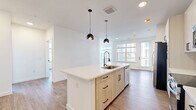Located in Austin, TX, this generously sized 3-bedroom, 2-bathroom single-story home offers a well-designed layout with modern finishes throughout. Light wood-tone flooring flows seamlessly across the open-concept living and kitchen area, creating a cohesive and inviting atmosphere. The kitchen is a standout feature, showcasing white cabinetry with matte black hardware, a large center island with a sink and pendant lighting, quartz countertops, stainless steel appliances, and a built-in beverage cooler. A dedicated entrance leads into the home, with a hallway connecting the bedrooms and common areas. The primary bedroom offers a comfortable retreat, with multiple windows that fill the space with natural light. Its en-suite bathroom is elegantly appointed with a dual-sink vanity, light wood cabinetry, a glass-enclosed walk-in shower with marble-style tile, and built-in shelving. The primary suite also includes a spacious walk-in closet with custom shelving and hanging rods. The additional bedrooms feature wood-look flooring and ample closet space with double doors. A dedicated laundry room houses a full-size washer and dryer. A private balcony offers views of the surrounding community and landscaped grounds, completing this well-appointed home.