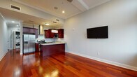 This single-floor residence combines classic architectural details with modern finishes throughout. Rich, polished cherry hardwood flooring flows seamlessly across the open living and kitchen areas, creating a warm and cohesive aesthetic. Crown molding and clean lines along the ceiling add a refined architectural touch.

The kitchen is a standout feature, outfitted with deep mahogany cabinetry, light granite countertops with natural veining, and a full suite of stainless steel appliances including a gas range, built-in microwave, and a French door refrigerator. A peninsula with an undermount sink and pendant lighting doubles as a prep and gathering space, opening directly to the living area.

The living area benefits from tall arched windows that flood the space with natural light and frame expansive city views, creating a bright and airy atmosphere. The elevated ceiling height enhances the sense of openness throughout.

The bathroom is thoughtfully designed with striking linear tile work on both the floors and walls in cool grey tones. A floating vanity with a marble-topped surface, framed mirror, and glass-enclosed shower contribute to its contemporary and polished character. The space as a whole offers a cohesive blend of warmth, elegance, and modern design sensibility.