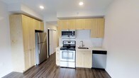 This well-appointed studio unit offers a practical and modern living experience within a compact, single-floor layout. The open-concept design maximizes the use of available space, seamlessly integrating the living and kitchen areas into one cohesive environment.

The kitchen is a standout feature, outfitted with a full suite of stainless steel appliances including a refrigerator, electric range with oven, over-the-range microwave, and dishwasher. Light natural wood cabinetry lines the walls, extending to the ceiling to provide generous storage capacity. The countertops are clean and minimal, complemented by a stainless steel sink. A subtle tile backsplash adds texture and visual interest behind the range.

The flooring throughout is a rich, dark hardwood-style material that grounds the space and contrasts beautifully with the light cabinetry and white walls. Recessed lighting in the ceiling provides bright, even illumination across the unit. A closet is accessible just off the kitchen area, offering additional storage. The unit includes one full bathroom.

Overall, the space presents a clean, modern aesthetic with functional finishes suited for efficient urban living.