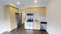 This well-appointed studio unit offers a practical and modern living experience within a compact, single-floor layout. The open-concept design maximizes the use of available space, seamlessly integrating the living and kitchen areas into one cohesive environment.

The kitchen is a standout feature, outfitted with a full suite of stainless steel appliances including a refrigerator, electric range with oven, over-the-range microwave, and dishwasher. Light natural wood cabinetry lines the walls, extending to the ceiling to provide generous storage capacity. The countertops are clean and minimal, complemented by a stainless steel sink. A subtle tile backsplash adds texture and visual interest behind the range.

The flooring throughout is a rich, dark hardwood-style material that grounds the space and contrasts beautifully with the light cabinetry and white walls. Recessed lighting in the ceiling provides bright, even illumination across the unit. A closet is accessible just off the kitchen area, offering additional storage. The unit includes one full bathroom.

Overall, the space presents a clean, modern aesthetic with functional finishes suited for efficient urban living.