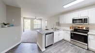 Located at 100 Patriot's Pointe Dr in Hillsborough, NC, this single-floor residence offers a well-designed, open layout with a neutral color palette and a blend of hardwood-style and carpeted flooring throughout. The kitchen serves as a central highlight, featuring white shaker cabinetry, granite countertops, a classic subway tile backsplash, stainless steel appliances including a range, over-the-range microwave, dishwasher, and refrigerator, and a peninsula that opens directly to the living area. The living room is bright and spacious, with large windows framing leafy outdoor views, a ceiling fan with light fixture, and plush carpeting underfoot. The bedrooms are generously proportioned, carpeted for comfort, and each includes closet storage. One room features hardwood-style flooring and a dedicated closet, offering flexibility as a bedroom or home office. The primary bathroom is appointed with white cabinetry, a large vanity mirror, modern light fixtures, and wood-look flooring, while the secondary bathroom includes a shower-tub combination and a clean white vanity. The overall ambiance is light, clean, and move-in ready, with consistent modern finishes that create a cohesive and comfortable living environment.