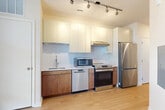 Located at 1100 Dahlia St NW, Unit 562 in Washington, DC, this one-bedroom, one-bathroom residence offers a thoughtfully designed layout across a single floor. Light wood flooring flows continuously throughout, creating a cohesive and clean aesthetic.

The kitchen is a standout feature, outfitted with a full suite of stainless steel appliances — including a range, dishwasher, refrigerator, and built-in microwave — complemented by warm wood lower cabinetry, crisp white upper cabinets, a white tile backsplash, and a single-basin sink. Track lighting overhead adds both functionality and a modern touch.

The combined dining and living area provides an open, flexible space filled with natural light from a window at the far end. A hallway connects the main living spaces to the bedroom, bathroom, closet, and laundry — keeping the layout organized and efficient.

The bedroom is a quiet, neutral-toned room with light wood flooring and a window allowing in natural light. The bathroom features light wood flooring, a warm wood vanity with a white countertop, an arched mirror, and clean white walls. In-unit laundry adds everyday convenience. The overall ambiance is modern, minimal, and move-in ready.