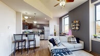 Located at 112 W Commerce St in Youngstown, Ohio, this 2-bedroom, 2-bathroom unit offers a well-designed single-floor layout that maximizes functionality. The open-concept living, dining, and kitchen area serves as the heart of the home, featuring light wood-style flooring, a ceiling fan, and large windows that flood the space with natural light and offer views of the surrounding cityscape and tree-lined streets. The kitchen is outfitted with rich dark wood cabinetry, dark countertops, a mosaic tile backsplash, and a full suite of stainless steel appliances including a refrigerator, range, microwave, and dishwasher. A breakfast bar with bar seating provides a casual dining option, while pendant lighting adds a polished touch overhead. Both bedrooms are carpeted and feature windows with outdoor views, offering a quiet retreat. The primary bedroom is a comfortable size, while the second bedroom provides additional flexibility. Each bathroom includes a vanity with dark wood cabinetry, a framed mirror, and a shower-tub combination. Two closets provide ample storage throughout the unit. The overall ambiance is modern and urban, with a clean, neutral palette complemented by thoughtful architectural details.