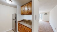 Located at 135 Ward St in Revere, Massachusetts, this single-floor residence offers a practical and well-organized layout. The kitchen is equipped with stainless steel appliances, including a refrigerator, electric range, and dishwasher. Warm-toned wood cabinetry provides generous storage above and below the granite-style countertops, while a decorative tile backsplash adds visual interest. Light tile flooring runs throughout the kitchen, which also features a range hood and an integrated sink. A peninsula counter with upper cabinetry connects the kitchen to the living area, creating an open, cohesive flow between the two spaces. The living area is spacious and bright, with soft carpeted flooring, neutral white walls, and a pendant light fixture that anchors the room. A sliding glass door allows natural light to filter in and provides access to an outdoor area. The bathroom is cleanly finished with tile flooring, a bathtub and shower combination, and brushed nickel hardware and fixtures. An intercom panel is conveniently located near the kitchen-living transition area. Overall, the unit presents a clean, functional living environment suited for everyday comfort.
