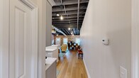 This one-bedroom, one-bathroom loft in Oxford, Michigan, blends industrial character with modern finishes across a single thoughtfully designed floor. The open living area makes an immediate impression with soaring exposed ceiling joists, visible ductwork, and pendant lighting that celebrate the space's raw architectural heritage. Original brick walls anchor the room with warmth and texture, while light hardwood flooring runs throughout, unifying the space with a clean, contemporary feel.

The kitchen is well-appointed with gray shaker-style cabinetry, white quartz countertops, a subway tile backsplash, and a full suite of stainless steel appliances including a gas range and French door refrigerator. A large central island with seating provides additional prep space and a natural gathering point.

The primary bathroom is elegantly finished with a wide vanity topped in quartz, gold-accented hardware, a framed mirror with modern sconce lighting, and a glass-enclosed walk-in shower with tile surround. A separate water closet adds additional privacy and functionality. A dedicated closet provides organized storage. Two hallways connect the private and common areas seamlessly. Natural light filters in through street-facing windows, complementing the industrial-chic aesthetic throughout this distinctive Oxford loft.