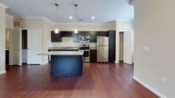 This single-floor residence offers a thoughtfully designed layout that balances open communal spaces with comfortable private quarters. The heart of the home is the kitchen, which features dark espresso cabinetry, granite countertops, a subway tile backsplash, and a full suite of stainless steel appliances including a range, microwave, dishwasher, and refrigerator. A built-in wine rack adds a distinctive touch, while a central island provides additional prep space and casual seating. Rich, dark hardwood flooring flows seamlessly through the kitchen and into the open living and dining areas, which are trimmed with elegant crown molding. The living room benefits from natural light through windows and features a ceiling fan, with a neutral accent wall adding warmth and depth to the space. A transom-topped entry door contributes to the bright, welcoming ambiance of the main living area. The bedrooms are carpeted for comfort and each include ceiling fans, generous windows that bring in natural light, and ample closet space. The bathroom is finished with granite countertops, dark vanity cabinetry, and a full tub-and-shower combination with tiled surround. Overall, the space presents a clean, modern aesthetic with consistent, quality finishes throughout.