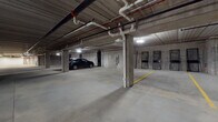 Located at 443 Duane St in Glen Ellyn, Illinois, this single-level enclosed parking garage offers a generously proportioned, functional space designed to accommodate multiple vehicles comfortably. The structure features a poured concrete construction throughout, with exposed concrete walls, support columns, and a ceiling that reveals an organized network of overhead piping, conduit, and mechanical systems running its full length.

The floor is a smooth concrete surface with yellow-painted striping that clearly delineates individual parking stalls and traffic flow areas, ensuring orderly use of the space. Artificial lighting is provided by ceiling-mounted fixtures distributed evenly throughout the garage, maintaining adequate visibility across all areas. The layout extends notably in depth, with multiple distinct parking zones visible from various vantage points within the structure.

Along the perimeter, access doors and storage cage enclosures are integrated into the concrete walls, providing utility and organizational options for occupants. A floor drain is centrally located, supporting proper water management within the enclosed environment. The garage's broad, open layout allows for ease of vehicle maneuvering. Overall, the space presents a clean, well-organized, and utilitarian parking environment suited for structured, secure vehicle storage.