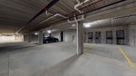 Located at 443 Duane St in Glen Ellyn, Illinois, this single-level enclosed parking garage offers a generously proportioned, functional space designed to accommodate multiple vehicles comfortably. The structure features a poured concrete construction throughout, with exposed concrete walls, support columns, and a ceiling that reveals an organized network of overhead piping, conduit, and mechanical systems running its full length.

The floor is a smooth concrete surface with yellow-painted striping that clearly delineates individual parking stalls and traffic flow areas, ensuring orderly use of the space. Artificial lighting is provided by ceiling-mounted fixtures distributed evenly throughout the garage, maintaining adequate visibility across all areas. The layout extends notably in depth, with multiple distinct parking zones visible from various vantage points within the structure.

Along the perimeter, access doors and storage cage enclosures are integrated into the concrete walls, providing utility and organizational options for occupants. A floor drain is centrally located, supporting proper water management within the enclosed environment. The garage's broad, open layout allows for ease of vehicle maneuvering. Overall, the space presents a clean, well-organized, and utilitarian parking environment suited for structured, secure vehicle storage.