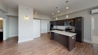 Located in the heart of Spartanburg, SC, this single-floor residence at 120 W Saint John St combines modern design with functional living. The open-concept layout connects the living area to a well-appointed kitchen, which features dark espresso cabinetry, granite-style countertops, a large center island with pendant lighting, and a full suite of stainless steel appliances including a refrigerator, range, microwave, and dishwasher. Rich wood-look flooring runs throughout the main living areas, adding warmth and continuity to the space. The living area benefits from large windows that flood the room with natural light and offer views of the surrounding Spartanburg cityscape. The bedrooms are generously sized, finished with plush carpeting, and fitted with large windows on multiple walls, maximizing natural light and urban views. Closet space is provided for convenient storage. Two full bathrooms mirror each other in design, each featuring dark vanity cabinetry with granite-style countertops, wood-look flooring, and a full tub-shower combination. The neutral gray palette throughout creates a clean, contemporary ambiance, while the thoughtful layout ensures a smooth flow between all areas of the residence.