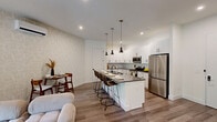 This thoughtfully designed one-bedroom, one-bathroom residence at 355 Broad St in Newark, NJ offers a well-appointed open-concept layout that maximizes every square foot. The combined kitchen and living area serves as the heart of the home, anchored by a large center island with a dark countertop and seating for multiple guests, illuminated by a trio of sleek pendant lights. Crisp white cabinetry, a tiled backsplash, and a full suite of stainless steel appliances — including a gas range, microwave, and refrigerator — complete the chef-friendly kitchen. A patterned accent wall adds visual interest to the dining and living zones, while wide-plank hardwood flooring runs throughout. The living area is bright and airy, with floor-to-ceiling sliding glass doors that open to an outdoor deck, inviting natural light and greenery views indoors. The bedroom is a serene retreat featuring large windows with outdoor views, textured wallcovering, dual closets, and a wall-mounted climate control unit. The bathroom offers a full tub-shower combination finished with large-format gray tile and matte black fixtures. Clean lines, modern hardware, and a neutral palette define the overall aesthetic of this well-crafted Newark residence.