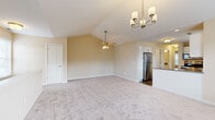 This two-floor home presents a well-organized layout with a cohesive neutral color palette of warm beige tones, white trim, and six-panel interior doors fitted with brushed nickel hardware throughout. The upper level showcases a spacious living area anchored by soaring vaulted ceilings, a ceiling fan, and an elegant chandelier. This open-concept space flows directly into the kitchen, which is outfitted with white shaker-style cabinetry, dark granite countertops, stainless steel appliances including a refrigerator, range, and microwave, and wood-look flooring. Natural light enters through white-blinded windows, enhancing the bright, airy atmosphere.

The bedrooms feature plush carpeting and ceiling fans, with windows dressed in horizontal blinds that allow for natural light. A full bathroom includes a tub-shower combination, a white vanity with granite countertops, and wood-look flooring. A dedicated laundry area houses a full-size washer and dryer beneath overhead cabinetry for added storage. The staircase landing, visible on the lower level, connects the floors with carpeted steps, and the surrounding hallways maintain the home's consistent, clean aesthetic.