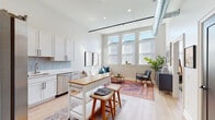 Located at 25 Raymond Ave in Poughkeepsie, NY, this single-floor loft-style residence blends industrial character with contemporary finishes throughout. The open-concept living and kitchen area is anchored by soaring ceilings with an exposed metal duct, recessed lighting, and a track rail system that add an unmistakable urban edge. Light oak hardwood flooring runs seamlessly throughout, complementing the airy, neutral palette.

The kitchen is well-appointed with crisp white shaker cabinetry, black hardware, a soft blue subway tile backsplash, light quartz countertops, and a full suite of stainless steel appliances. A freestanding butcher block island provides additional prep space and casual seating. The living area benefits from a generous bank of windows that flood the space with natural light.

The primary bedroom is a standout, featuring a dramatic exposed brick accent wall that rises to the full ceiling height, lending warmth and texture. A second bedroom offers a clean, tranquil retreat. The bathroom is finished with penny tile flooring, a warm wood vanity, white quartz countertop, and a glass-enclosed walk-in shower. An in-unit stacked washer and dryer adds everyday convenience.