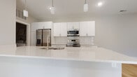 Located at 5101 Magnolia Lake Dr. in Westerville, Ohio, this single-floor home offers a clean, modern aesthetic throughout its well-appointed layout. The kitchen is a standout feature, showcasing sleek white cabinetry, quartz countertops with subtle speckled detailing, a classic white subway tile backsplash, and a full suite of stainless steel appliances including a French door refrigerator, electric range with microwave, and dishwasher. Pendant lighting accents the generous island with an integrated sink, creating an ideal space for both cooking and casual dining. Light hardwood-style flooring runs through the main living and kitchen areas, lending warmth and continuity to the open floor plan. The living area is bright and spacious, with recessed lighting and sliding glass doors that invite natural light. Bedrooms are finished with soft wall-to-wall carpeting, large windows providing neighborhood views, and closets with built-in shelving for convenient storage. The bathroom features a white vanity with quartz countertop, dark tile flooring, brushed nickel fixtures, and a full soaking tub with shower. A dedicated laundry room with washer and dryer hookups and a water heater adds practical convenience to this thoughtfully designed home.