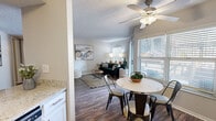 This thoughtfully designed 2-bedroom, 2-bathroom residence offers a comfortable and functional single-floor layout. The open-plan living, dining, and kitchen area forms the heart of the home, featuring durable wood-style flooring, a textured ceiling, and ceiling fans that enhance air circulation throughout. Large windows fitted with blinds allow generous natural light to fill the space while maintaining privacy.

The kitchen is well-equipped with stainless steel appliances, including a range, microwave, and refrigerator. Crisp white shaker cabinetry, granite countertops, a subway tile backsplash, and a double stainless steel sink complete the space with a clean, modern aesthetic. An in-unit washer and dryer are conveniently tucked nearby. The adjacent dining area comfortably accommodates a round table, creating an inviting spot for daily meals.

The primary bedroom offers plush carpeting, a sliding-door closet, and a natural window, providing a calm and restful retreat. The second bedroom is similarly comfortable with its own closet and window. Two full bathrooms with hard-surface flooring and natural light serve the residence.

Outside, a staircase leads to a shared community area featuring a pool, iron fencing, and mature trees, offering a pleasant outdoor escape.