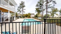 Situated in Myrtle Beach, South Carolina, this single-story property at 1500 Coastal Lane offers a welcoming coastal lifestyle complemented by well-maintained outdoor amenities. The standout feature of this space is its outdoor swimming pool, which is generously sized and surrounded by a clean, expansive concrete deck ideal for lounging and entertaining. The pool area is enclosed by a sturdy black iron fence, providing both safety and a polished aesthetic. Lounge chairs are positioned poolside, offering comfortable spots to relax and enjoy the outdoors. Mature pine and deciduous trees frame the perimeter of the pool area, providing natural shade and a sense of privacy while contributing to the serene, park-like atmosphere. The lush greenery surrounding the property enhances its coastal charm and creates a peaceful retreat from the nearby neighborhood. The property's single-floor layout promotes ease of accessibility throughout. Overall, this space combines functional outdoor living with a tranquil natural setting, making it well-suited for those seeking a relaxed, amenity-rich environment in the heart of Myrtle Beach.
