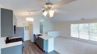 This single-floor residence showcases a thoughtfully designed open-concept layout where the kitchen and living areas flow seamlessly together. The kitchen is well-appointed with gray shaker-style cabinetry, light quartz countertops, and a full suite of stainless steel appliances, including a gas range, microwave, and refrigerator. A peninsula with an undermount sink provides additional prep space and serves as a natural divider between the kitchen and the adjoining living area. An elegant drum chandelier and a ceiling fan with light kit provide both ambient and functional lighting throughout this shared space.

The living area features vaulted ceilings that enhance the sense of openness, plank-style hardwood flooring that transitions to plush carpet, and a sliding glass door fitted with vertical blinds that invites generous natural light. Additional rooms include carpeted bedrooms with windows offering outdoor views, and a spacious walk-in closet outfitted with wire shelving and hanging rods for ample storage. The bathroom features a tub-shower combination with white square tile surround, chrome fixtures, and a curved shower rod. Throughout the space, neutral tones and clean finishes create a bright, move-in-ready atmosphere.