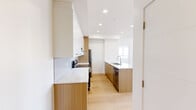 Located at 110 Lucas St NW in Calgary, Alberta, this well-appointed 2-bedroom, 2-bathroom unit offers a thoughtfully designed single-level layout. The open-concept kitchen serves as the heart of the home, featuring a large central island with an undermount sink, crisp white upper cabinetry paired with warm wood-toned lower cabinets, light stone countertops, a subway tile backsplash, and stainless steel appliances including a fridge and electric range. Light hardwood flooring runs throughout, complementing the bright, clean aesthetic of every room. Both bedrooms are comfortably sized, each featuring large sliding windows that bring in natural light and offer views of the surrounding developing neighbourhood. The two bathrooms are finished consistently with wood-toned vanities, white countertops, full soaker tub-shower combinations, and recessed lighting. A hallway connects the living spaces efficiently. The unit also includes a private balcony with a wood-panelled ceiling, metal railings, and open views of the emerging Calgary community beyond. Recessed pot lights and baseboard heaters are found throughout, reflecting a practical and modern interior finish suited for comfortable everyday living.