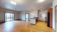 Located at 500 E Michigan Ave in Lansing, Michigan, this single-floor residence offers a thoughtfully designed open-concept layout with a seamless flow between the living and kitchen areas. The expansive main living space is finished with warm bamboo hardwood flooring that extends throughout, complemented by neutral-toned walls and ample overhead lighting, including a track lighting system and elegant pendant lights above the kitchen island.

The kitchen is well-equipped, featuring rich cherry wood cabinetry, dark granite countertops, and black appliances including an electric range with built-in microwave. A central island with a sink and additional storage provides both functionality and a natural division between the kitchen and the open living area. A sliding glass door in the living room leads to an outdoor balcony, inviting natural light into the space.

The bedrooms are carpeted for comfort and are served by tall windows fitted with blinds, allowing for adjustable natural light. The bathroom includes a full tub-shower combination, a toilet, and a vanity with a solid-surface countertop and cherry wood cabinetry beneath a large mirror. A separate vanity area provides added convenience. The unit's clean, contemporary finishes and efficient floor plan make it a practical and comfortable urban residence.