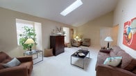 This single-floor residence offers a thoughtfully designed layout with distinct living zones that flow naturally from one space to the next. The main living area is a standout, featuring vaulted ceilings and a large rectangular skylight that floods the carpeted space with natural light. Neutral warm-toned walls and generous square footage create an open, airy atmosphere, complemented by a secondary seating area with a wall-mounted television.

The dining room features rich hardwood flooring, warm neutral walls, and an elegant chandelier overhead, providing a refined space for formal meals. Adjacent to the dining area, the kitchen is equipped with ample white cabinetry trimmed in warm wood tones, generous counter space, and hardwood flooring, providing a practical and well-organized cooking environment with full appliances.

The bedrooms are carpeted and spacious, each with vaulted ceilings that enhance the sense of volume. The primary bedroom includes double doors opening to a walk-in closet and an en-suite bathroom featuring a wide dual-sink vanity with oak cabinetry, a large mirror, and tile flooring. Throughout the home, a cohesive neutral palette and consistent architectural details create a calm, comfortable ambiance.