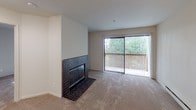 This well-appointed 1-bedroom, 1-bathroom unit is contained entirely on a single floor, offering a functional and comfortable layout. The living room serves as the centerpiece of the home, highlighted by a striking floor-to-ceiling tile-surround fireplace with a dark mosaic tile finish that anchors the space with a classic touch. Large sliding glass doors open to a private balcony, framing lush outdoor greenery and allowing natural light to pour in through vertical blinds. Plush carpet flooring extends throughout the main living areas, adding warmth underfoot, while baseboard heating units along the walls ensure year-round comfort. The bedroom is a bright, quiet retreat featuring a large window with vertical blinds that invite natural light while offering privacy, along with carpeted floors and a ceiling fan for added convenience. The bathroom is efficiently designed with light tile flooring, a sliding glass-door tub and shower combination, and textured walls that add subtle dimension to the space. Grab bars are thoughtfully incorporated for added accessibility. The overall layout, as seen in the overhead model, is compact yet practical, with clearly defined spaces and a neutral color palette throughout that creates a clean, airy ambiance well-suited for comfortable everyday living.