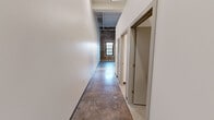 Located at 601 W 2nd St in Davenport, Iowa, this one-bedroom, two-bathroom unit spans two floors, offering a distinctive blend of industrial character and contemporary updates. The main floor comprises the bulk of the living space, featuring a well-equipped kitchen with warm wood cabinetry, granite countertops, a central island, and stainless steel appliances including a refrigerator, range, microwave, and dishwasher. Exposed ductwork on the ceiling adds an industrial aesthetic throughout. Terrazzo flooring is found in several areas, contributing to the building's unique, converted character. Two bathrooms are present — one with a walk-in shower and granite-topped vanity, and another equally well-finished half bath. The upper level, accessed via stairway, features the bedroom with carpeted flooring, exposed piping overhead, and a small window. A standout feature is the upper-level area showcasing original brick walls, black-framed industrial windows with views to the street, vaulted white-painted wood plank ceilings, and exposed structural beams — a nod to the building's historic origins. A hallway, closet, and ceiling fans throughout round out this character-rich, thoughtfully updated urban residence.