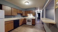 Located at 525 E Main St in Ravenna, Ohio, this single-floor unit offers a practical and well-organized layout suited for comfortable everyday living. The kitchen is equipped with warm wood-toned cabinetry, light countertops, a white electric range, a black dishwasher, and an under-cabinet range hood. A pass-through window connects the kitchen to the main living area, promoting an open, communicative flow between the two spaces. The living area is generously sized, featuring wood-look vinyl plank flooring, cool blue-gray painted walls, and a window that brings in natural light. A wall-mounted air conditioning unit and baseboard heating provide year-round climate control. The bedrooms are carpeted and painted in coordinating deep blue-gray tones, each featuring windows with blinds that allow for natural light and outdoor views. One bedroom includes a double bifold closet offering ample storage space, while another benefits from two windows for added brightness. Baseboard heating is present throughout the bedrooms as well. The consistent use of wood-look flooring in the main living areas and carpet in the bedrooms, combined with the cohesive cool-toned color palette, gives the unit a unified and tidy aesthetic throughout.