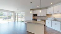 This single-floor unit at 5445–5499 Congress Ave in Madison, WI presents a clean, contemporary design with an open-concept layout that maximizes functionality and natural light. The kitchen serves as the centerpiece of the living space, featuring white shaker cabinetry with brushed nickel hardware, granite countertops, a subway tile backsplash, and a full suite of stainless steel appliances including a gas range, microwave, dishwasher, and refrigerator. A central island with a matching granite surface provides additional prep space and is illuminated by pendant lighting overhead. The kitchen flows seamlessly into the living area, which is finished with durable wood-look flooring and benefits from abundant natural light streaming through large sliding glass doors that open to outdoor views of the surrounding greenery. The bedrooms are carpeted for comfort and feature ceiling fans, natural wood trim, and windows that frame pleasant outdoor scenery. The bathroom is well-appointed with a granite vanity, a tub-shower combination, and wood-look flooring. A dedicated laundry area with full-size washer and dryer units adds practical convenience. Throughout, neutral tones and clean lines create a bright, cohesive ambiance.