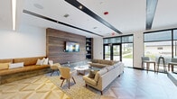 Located on Space Age Road in Madison, Alabama, this contemporary single-floor amenity space is thoughtfully designed to balance social engagement with relaxed comfort. The interior showcases a striking geometric-patterned floor in light wood tones that flows throughout, creating a cohesive visual foundation across all areas of the space.

The lounge area serves as a welcoming focal point, anchored by a full-width reclaimed wood accent wall fitted with a wall-mounted flat-screen television and flanked by navy-toned open shelving. Plush neutral sectional sofas, mid-century-inspired accent chairs, and a round coffee table create an inviting gathering space. A built-in L-shaped leather banquette nook with decorative pillows offers an intimate seating alternative nearby.

The recreation zone features a full-size billiards table positioned beneath a bold sputnik-style chandelier, providing dramatic overhead lighting. A deep teal accent wall adds a pop of color, complemented by framed artwork and a cue rack. High-top bistro tables and bar seating line the floor-to-ceiling window wall, flooding the space with natural light and offering unobstructed views of the landscaped outdoor courtyard, seamlessly connecting the interior to the vibrant surroundings outside.