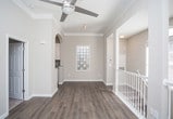 This two-story home offers a thoughtfully designed interior that balances openness with defined living areas. The main level features warm hardwood-style flooring that flows seamlessly throughout, complemented by crisp white trim and elegant crown molding that adds a refined architectural detail to every room. Natural light pours in through large windows, creating a bright and inviting atmosphere.

A central hallway connects the main living spaces, with a graceful arched entryway leading into the kitchen area. The kitchen is equipped with modern stainless steel appliances, including a refrigerator and range, set against dark cabinetry that provides a striking contrast to the light-toned walls. Recessed lighting above ensures the space is well-lit and functional.

Structural columns add a subtle architectural character to the open hallway area, while a staircase with white balusters provides access between the two floors. Neutral, warm-toned walls throughout lend the home a cohesive and welcoming ambiance. Doorways open to additional rooms featuring plush carpeting, offering a comfortable transition from the hard-surface common areas. Overall, the space presents a clean, move-in-ready aesthetic with classic design elements and a practical, flowing layout.