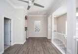 This two-story home offers a thoughtfully designed interior that balances openness with defined living areas. The main level features warm hardwood-style flooring that flows seamlessly throughout, complemented by crisp white trim and elegant crown molding that adds a refined architectural detail to every room. Natural light pours in through large windows, creating a bright and inviting atmosphere.

A central hallway connects the main living spaces, with a graceful arched entryway leading into the kitchen area. The kitchen is equipped with modern stainless steel appliances, including a refrigerator and range, set against dark cabinetry that provides a striking contrast to the light-toned walls. Recessed lighting above ensures the space is well-lit and functional.

Structural columns add a subtle architectural character to the open hallway area, while a staircase with white balusters provides access between the two floors. Neutral, warm-toned walls throughout lend the home a cohesive and welcoming ambiance. Doorways open to additional rooms featuring plush carpeting, offering a comfortable transition from the hard-surface common areas. Overall, the space presents a clean, move-in-ready aesthetic with classic design elements and a practical, flowing layout.