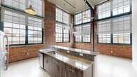 Located at 57 Charter Oak Ave in Hartford, CT, this 2-bedroom, 3-bathroom loft-style residence masterfully blends industrial character with modern finishes. The open living area commands immediate attention with its soaring ceilings, dramatic floor-to-ceiling multi-pane windows framed in deep green, and original exposed brick walls that flood the space with natural light and urban charm. Light-toned concrete-style flooring runs throughout, complementing the raw architectural aesthetic.

The kitchen is a standout feature, anchored by a generous granite-topped island with an undermount sink, rich wood-grain cabinetry extending to the full height of the dramatic ceilings, and a complete suite of stainless steel appliances including a refrigerator, range, and built-in microwave. Industrial pendant lighting adds warmth overhead.

The spacious primary bedroom continues the loft aesthetic with exposed brick accents and large windows offering urban views. The two additional bedrooms provide comfortable, well-proportioned spaces with access to natural light. Three bathrooms feature consistent finishes, including granite-topped vanities with wood cabinetry and clean, white-tiled shower stalls with brushed nickel fixtures. A wide hallway connects the private quarters, completing this thoughtfully designed urban retreat.