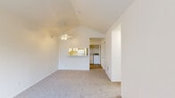 Located at 4505 SW Masters Loop in Beaverton, Oregon, this one-bedroom, one-bathroom residence offers a well-organized single-floor layout designed for comfortable everyday living. The living area is a standout feature, showcasing soaring vaulted ceilings accented by a ceiling fan, creating an airy and open atmosphere. Plush carpet runs throughout the living room and bedroom, adding warmth underfoot. A pass-through window connects the living area to the kitchen, promoting an open, connected feel. The kitchen is efficiently laid out with white cabinetry trimmed in warm wood tones, a white electric range, a stainless steel sink, and ample counter space, all set on durable tile flooring. The bedroom is generously sized, featuring neutral carpet, a window with vertical blinds that allows natural light and outdoor views, and a baseboard heater. The bathroom includes a single-sink vanity with wood-accented cabinetry, a large mirror with overhead lighting, and tile flooring. A dedicated in-unit laundry area accommodates a full-size washer and dryer, adding everyday convenience. Additional storage is provided via a hallway closet. The overall aesthetic is clean and neutral throughout, offering a functional and move-in ready living space.