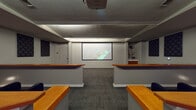 This single-floor screening room is thoughtfully designed to deliver an immersive audio-visual experience. The space is anchored by a large projection screen at the front wall, paired with a ceiling-mounted projector that ensures high-quality image display for presentations, film screenings, or media events. Tiered wooden platforms divide the room into distinct viewing levels, each accommodating rows of dark upholstered seating that offer clear sightlines to the screen from every position. A striking red circular lounge seat adds a bold accent and provides an informal seating option along the side of the room. Acoustic treatment is a central design feature, with multiple diamond-quilted sound-absorbing panels mounted strategically across the walls to optimize audio clarity and minimize unwanted reverberation. The ceiling incorporates a recessed cove lighting system that casts a soft, ambient glow throughout the space, complementing the subdued, theater-like atmosphere. Neutral grey carpeting covers the floor throughout, contributing to both the acoustic performance and the refined aesthetic. A small built-in cabinetry unit near the front of the room provides additional functionality. The overall ambiance is polished and professional, making this space well-suited for media screenings, corporate presentations, or private entertainment.