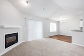 This single-floor residence offers a thoughtfully designed layout that balances comfort and functionality. The living room serves as a central highlight, featuring vaulted ceilings that lend an airy, open feel, soft carpeting underfoot, and a sleek fireplace set against a clean white surround. A sliding glass door with vertical blinds opens to the outdoors, while an adjacent window allows natural light to fill the space. A chandelier accents the transition toward the dining area, which flows into the kitchen via a peninsula with a dark countertop overhang.

The kitchen is well-appointed with crisp white cabinetry, white subway tile backsplash, dark countertops, and wood-look flooring. Black appliances, including a range, dishwasher, refrigerator, and built-in microwave, provide a cohesive look. A window above the counter brings in additional natural light.

The bedrooms are carpeted and generously proportioned, with one room featuring an arched window and a baseboard heater. The primary bathroom includes a wide vanity with a framed mirror and access to a walk-in closet. A secondary bathroom features wood-look flooring, a combined tub and shower, and a dark-countered vanity. A hallway connects the private areas of the home with clean, neutral finishes throughout.