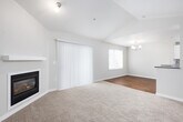 This single-floor residence offers a thoughtfully designed layout that balances comfort and functionality. The living room serves as a central highlight, featuring vaulted ceilings that lend an airy, open feel, soft carpeting underfoot, and a sleek fireplace set against a clean white surround. A sliding glass door with vertical blinds opens to the outdoors, while an adjacent window allows natural light to fill the space. A chandelier accents the transition toward the dining area, which flows into the kitchen via a peninsula with a dark countertop overhang.

The kitchen is well-appointed with crisp white cabinetry, white subway tile backsplash, dark countertops, and wood-look flooring. Black appliances, including a range, dishwasher, refrigerator, and built-in microwave, provide a cohesive look. A window above the counter brings in additional natural light.

The bedrooms are carpeted and generously proportioned, with one room featuring an arched window and a baseboard heater. The primary bathroom includes a wide vanity with a framed mirror and access to a walk-in closet. A secondary bathroom features wood-look flooring, a combined tub and shower, and a dark-countered vanity. A hallway connects the private areas of the home with clean, neutral finishes throughout.