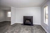 This single-floor residence offers a clean, functional layout with consistent finishes throughout. The living area is generously sized, bathed in natural light from multiple windows fitted with blinds, and anchored by a striking black-tiled fireplace that serves as a focal point. Crown molding lines the ceiling, adding a refined touch, while light gray wood-look flooring flows seamlessly across the space.

The kitchen is thoughtfully designed with white cabinetry, granite-style countertops, and a peninsula that opens toward the main living area, creating an efficient and connected layout. Black appliances — including a refrigerator, gas range, microwave, and dishwasher — provide a bold contrast against the bright cabinetry and counters. Recessed lighting and under-cabinet lighting enhance visibility and ambiance.

The bathroom is accessed via a hallway flanked by doors, offering a sense of privacy. It features a white vanity with granite-style countertops, a well-lit mirror with overhead bar lighting, and light hardwood-style flooring that coordinates with the rest of the unit.

Throughout the space, neutral gray walls, white trim, and textured ceilings contribute to a cohesive, understated aesthetic that provides a versatile backdrop for a variety of interior styles.