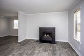 This single-floor residence offers a clean, functional layout with consistent finishes throughout. The living area is generously sized, bathed in natural light from multiple windows fitted with blinds, and anchored by a striking black-tiled fireplace that serves as a focal point. Crown molding lines the ceiling, adding a refined touch, while light gray wood-look flooring flows seamlessly across the space.

The kitchen is thoughtfully designed with white cabinetry, granite-style countertops, and a peninsula that opens toward the main living area, creating an efficient and connected layout. Black appliances — including a refrigerator, gas range, microwave, and dishwasher — provide a bold contrast against the bright cabinetry and counters. Recessed lighting and under-cabinet lighting enhance visibility and ambiance.

The bathroom is accessed via a hallway flanked by doors, offering a sense of privacy. It features a white vanity with granite-style countertops, a well-lit mirror with overhead bar lighting, and light hardwood-style flooring that coordinates with the rest of the unit.

Throughout the space, neutral gray walls, white trim, and textured ceilings contribute to a cohesive, understated aesthetic that provides a versatile backdrop for a variety of interior styles.