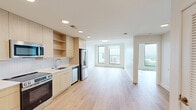 Located in the heart of Raleigh, NC, this modern one-bedroom, one-bathroom residence offers a thoughtfully designed open-concept layout with a clean, contemporary aesthetic throughout. Light-toned hardwood floors run seamlessly across the entire living space, complementing the crisp white walls and creating a bright, airy atmosphere.

The combined kitchen, dining, and living area forms the central hub of the home. The kitchen features flat-front light wood cabinetry with open shelving, white quartz countertops, a white tile backsplash, and a full suite of stainless steel appliances including a range, microwave, dishwasher, and French door refrigerator. Recessed lighting illuminates the space efficiently.

Floor-to-ceiling windows in both the living area and bedroom frame sweeping elevated views of the Raleigh skyline and surrounding greenery, flooding the interior with abundant natural light. The bedroom is a comfortable, well-proportioned retreat with large windows and a dedicated closet.

The bathroom maintains the same modern design language, featuring light wood vanity cabinetry, a white countertop with an undermount sink, an LED-backlit mirror, and neutral tile flooring. The unit also includes a dedicated laundry area and utility space, rounding out the functional layout of this refined urban residence.