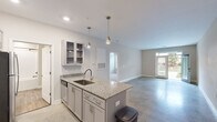 Located at 141 Stobhill Ln in Fuquay-Varina, NC, this thoughtfully designed one-bedroom, one-bathroom home offers a comfortable and modern living experience across a single floor. The open-concept layout creates a seamless flow between the kitchen and living area, anchored by polished concrete floors that lend an industrial-chic aesthetic throughout the main space.

The kitchen is a standout feature, equipped with granite countertops, gray shaker-style cabinetry with glass-front upper cabinets, stainless steel appliances including a range with a wall-mounted hood, a built-in microwave, and a refrigerator. A peninsula with an undermount sink and pendant lighting above adds both functionality and style. Natural light pours in through a glass-panel front door, brightening the open living area.

The bedroom is a generously sized retreat, carpeted for comfort and outfitted with a ceiling fan and dual windows that invite in natural light and outdoor views. It connects directly to a walk-in closet with wire shelving and to the full bathroom, which features a tiled tub-shower combination with sleek matte black fixtures. The entrance provides a welcoming transition into the home, completing this well-appointed and efficiently designed single-story residence.
