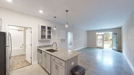 Located at 141 Stobhill Ln in Fuquay-Varina, NC, this thoughtfully designed one-bedroom, one-bathroom home offers a comfortable and modern living experience across a single floor. The open-concept layout creates a seamless flow between the kitchen and living area, anchored by polished concrete floors that lend an industrial-chic aesthetic throughout the main space.

The kitchen is a standout feature, equipped with granite countertops, gray shaker-style cabinetry with glass-front upper cabinets, stainless steel appliances including a range with a wall-mounted hood, a built-in microwave, and a refrigerator. A peninsula with an undermount sink and pendant lighting above adds both functionality and style. Natural light pours in through a glass-panel front door, brightening the open living area.

The bedroom is a generously sized retreat, carpeted for comfort and outfitted with a ceiling fan and dual windows that invite in natural light and outdoor views. It connects directly to a walk-in closet with wire shelving and to the full bathroom, which features a tiled tub-shower combination with sleek matte black fixtures. The entrance provides a welcoming transition into the home, completing this well-appointed and efficiently designed single-story residence.