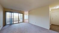 This single-floor unit offers a practical and comfortable layout designed to maximize livability. The main living area is generously sized, featuring plush wall-to-wall carpeting and neutral, warm-toned walls that create a bright and inviting atmosphere. A sliding glass door opens directly to a private patio, flooding the space with natural light and providing easy access to the outdoors. Vertical blinds offer privacy and light control throughout the living and adjoining areas.

A ceiling fan is centrally positioned in the living space, adding both function and a subtle decorative touch. The layout flows naturally into additional carpeted rooms, each well-proportioned and filled with natural light from large windows. These versatile rooms offer ample space for a variety of uses.

The kitchen is a standout feature, outfitted with dark cabinetry, light stone-look countertops, and a suite of black appliances including a gas range, built-in microwave, and refrigerator. Light wood-look vinyl flooring extends through the kitchen and into the bathroom, providing a clean, durable surface.

The bathroom is efficiently designed with a white vanity, a tub-shower combination, and the same wood-look vinyl flooring, creating a cohesive and tidy finish throughout the unit.