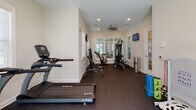 Located at 3973 Woolcock Dr in Myrtle Beach, SC, this single-floor fitness center is thoughtfully designed to support a comprehensive workout experience. The space is finished with dark rubberized flooring throughout, providing a durable and functional surface suited for a wide range of exercise activities. Neutral-toned walls and recessed lighting create a clean, bright environment, while multiple white-framed windows fitted with blinds allow generous natural light to fill the room. A ceiling fan aids in air circulation during intense workouts.

The cardio zone is equipped with multiple True-brand treadmills and an elliptical machine, all positioned to take advantage of the natural light from surrounding windows. A wall-mounted television is conveniently positioned for entertainment during cardio sessions. The strength training area features a multi-station cable machine, an adjustable workout bench, and a full rack of dumbbells ranging across various weight increments. A dedicated cycling station includes an air resistance bike, ideal for high-intensity interval training. Additional equipment such as medicine balls on a wall-mounted rack and resistance accessories rounds out the offerings. French doors with glass panels open to an outdoor view, enhancing the sense of openness throughout the space.
