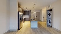 Located in the heart of Raleigh, NC, this single-floor unit at 119 S Harrington St offers a thoughtfully designed, modern living space with clean lines and contemporary finishes throughout. The open-concept layout flows naturally from the kitchen into the living areas, creating a cohesive and functional environment. The kitchen is a standout feature, showcasing flat-panel, wood-toned cabinetry, a white subway tile backsplash, sleek quartz countertops, and a full suite of stainless steel appliances including a refrigerator with ice maker, electric range, and built-in microwave. A central island with a undermount sink and pendant lighting above adds both practicality and style, while track lighting illuminates the space. Light wood-tone luxury vinyl flooring runs consistently throughout, lending warmth and continuity. The bedroom is well-proportioned with dual windows offering views of the surrounding neighborhood and a ceiling fan for comfort. The bathroom is long and efficiently laid out, featuring a wood-toned vanity with a white countertop, framed mirror, and a tub-shower combination with white tile surround. Additional utility is provided by a dedicated storage or laundry closet equipped with overhead shelving and an access panel, completing this well-appointed urban residence.