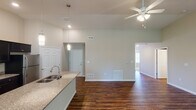 This single-floor residence offers a thoughtfully designed open-concept layout that seamlessly connects the kitchen, dining, and living areas. The kitchen is a standout feature, equipped with dark espresso cabinetry, granite countertops, stainless steel appliances including a refrigerator, microwave, and range, and a center island with a built-in sink and pendant lighting overhead. Rich, dark hardwood-style flooring flows throughout the main living areas, adding warmth and visual continuity.

The spacious living area benefits from soaring ceilings, a ceiling fan, and a sliding glass door that fills the room with natural light and provides outdoor access. Neutral warm-toned walls create a clean, inviting ambiance throughout.

The bedrooms are carpeted for comfort, each featuring ceiling fans or flush-mount lighting and window blinds that allow for ample natural light. The primary bathroom offers a walk-in shower, dark vanity cabinetry with granite countertops, and hardwood-style flooring, while the secondary bathroom features a full soaking tub and shower combination with similar finishes. A walk-in closet is accessible from the primary bath, adding practical storage. The overall design balances modern finishes with functional, comfortable living spaces.