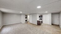 Located at 2030 Generals Way in Dover, Delaware, this single-floor unit offers a practical and well-designed layout across a compact but functional footprint. The main living area is an open, carpeted space finished in neutral gray tones with a textured ceiling and recessed flush lighting throughout. Windows fitted with blinds allow natural light to filter in, and a wall-mounted HVAC unit provides climate control. The flooring transitions from plush carpet in the living zone to wood-look vinyl planking in the kitchen and utility areas, creating a clear and clean delineation between spaces. The kitchen is efficiently designed in a galley-style configuration, featuring gray cabinetry, a light quartz countertop, a stainless steel sink with a pull-down faucet, and a full suite of stainless steel appliances including a refrigerator, dishwasher, electric range, and over-the-range microwave. An electrical panel is conveniently housed within the kitchen. A dedicated laundry area includes a stacked washer and dryer unit, adding significant convenience. The bathroom is clean and straightforward, featuring wood-look flooring, a tub and shower combination, and crisp white fixtures throughout. The overall aesthetic is modern, minimal, and move-in ready.