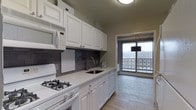 Located at 25 Washington Lane in Wyncote, Pennsylvania, this single-floor residence offers a thoughtfully designed living space with clean, contemporary finishes throughout. The kitchen is a standout feature, showcasing crisp white cabinetry with classic raised-panel detailing that extends from counter to ceiling, maximizing storage capacity. A dark gray subway tile backsplash provides a stylish contrast against the white surfaces, while light-toned countertops and wood-look flooring add warmth and cohesion. The kitchen is equipped with a gas range, built-in microwave, dishwasher, and a stainless steel sink beneath a modern arc-style faucet. Flush ceiling lighting keeps the space bright and functional. Adjacent to the kitchen, an enclosed balcony area — framed by a large window and decorative lattice railing — brings in natural light and offers views of the surrounding winter landscape. A pendant light fixture with a dark shade adds an accent of style to this transitional space. The overall ambiance of the residence is clean, neutral, and move-in ready, with a palette of whites, grays, and warm wood tones creating a cohesive and welcoming atmosphere throughout.